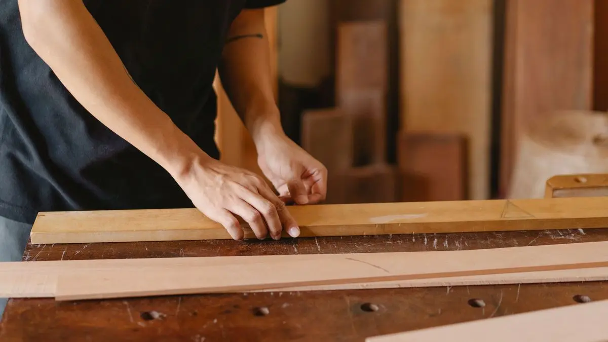 Hände richten an einer alten Hobelbank Holzleisten aus, das Gesicht ist nicht zu sehen – Arbeit in der Werkstatt