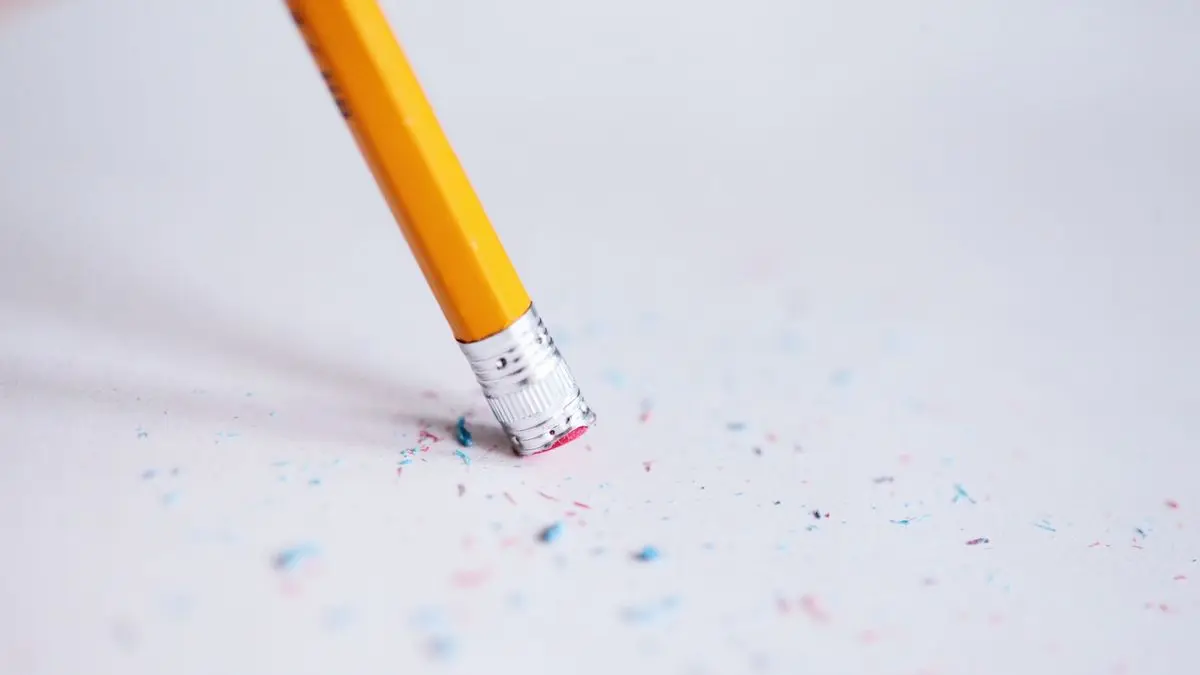Gelber Bleistift radiert mit dem Radiergummi auf weißem Papier, ringsum liegen Radierkrümel