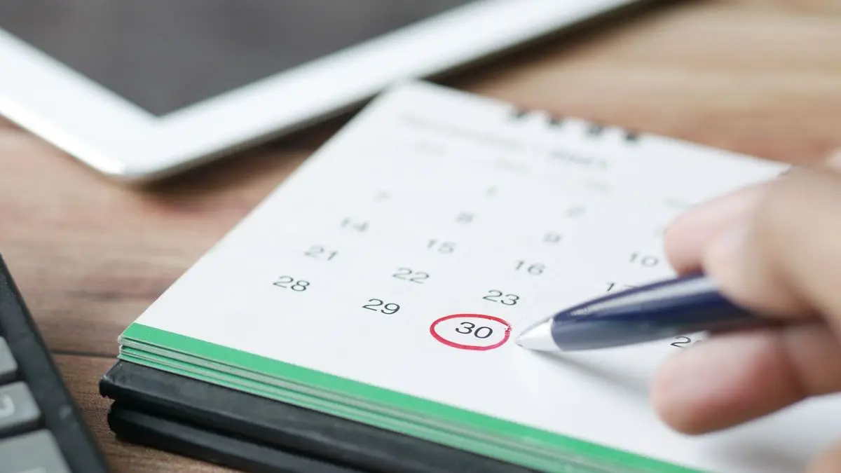 Hand mit Kugelschreiber, auf einem Tischkalender ist der 30. rot eingekreist